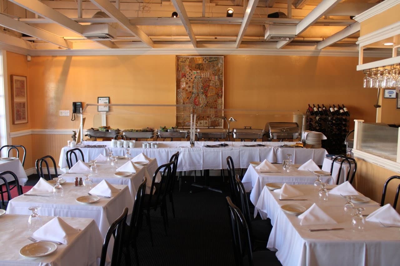 Jaipur Cuisine of India's dining room: white tablecloths and folded napkins, the buffet line along the back wall, and a tapestry on warm yellow paint.