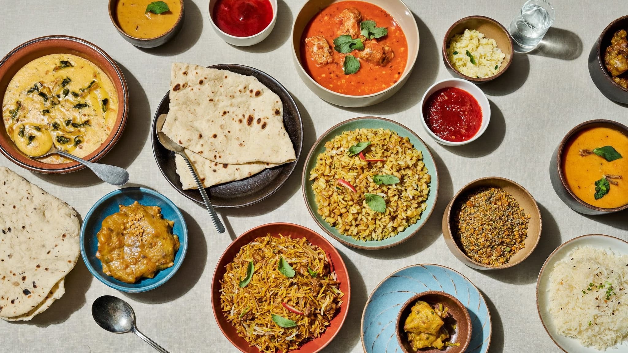 A table spread of Indian dishes: curries, naan, biryani, rice, and chutneys on linen.
