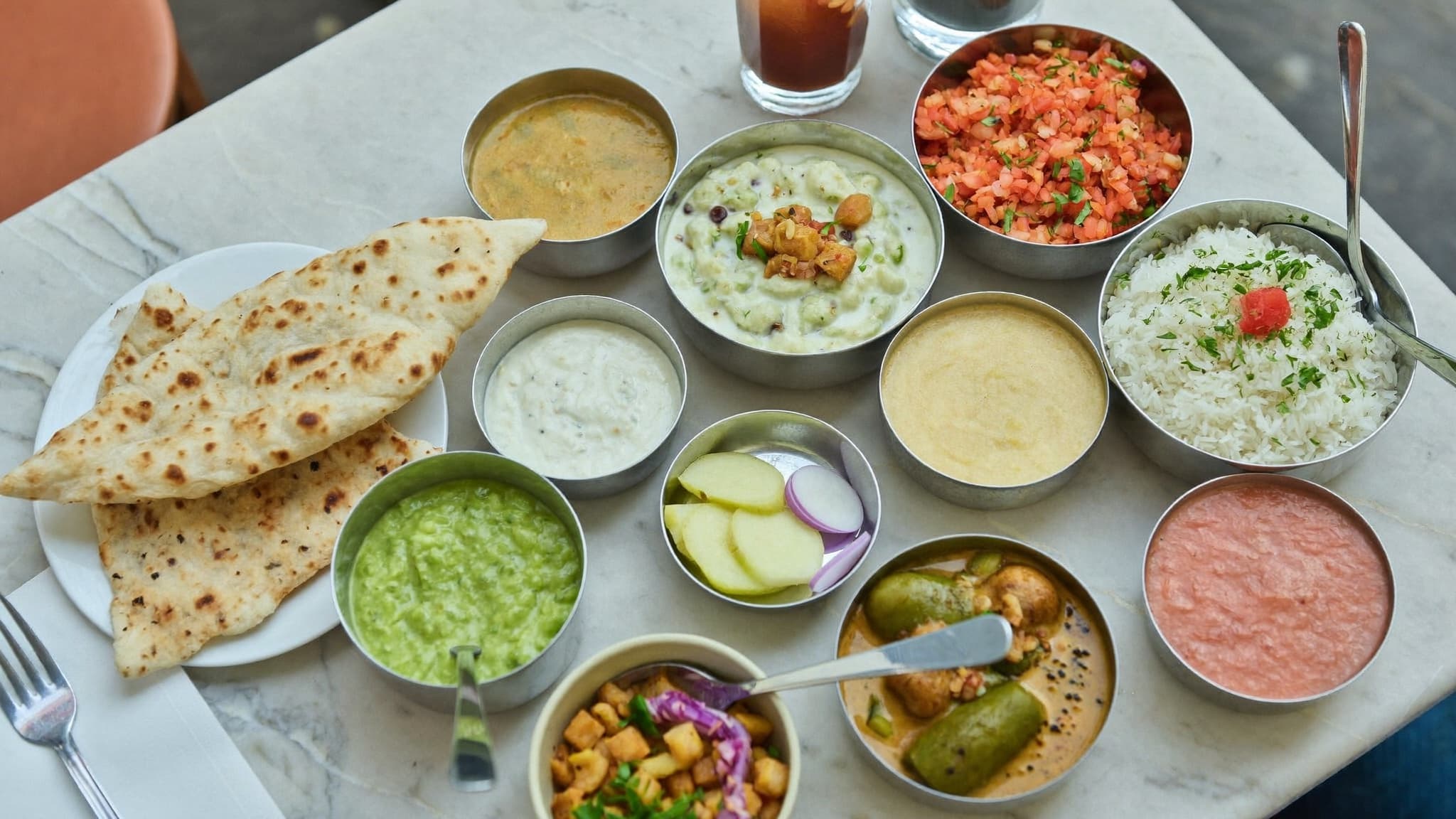 A thali platter of curries, dal, rice, and naan on soft linen, seen from above.
